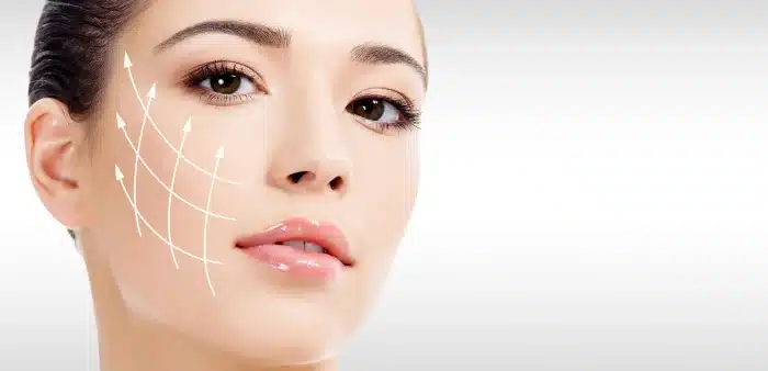 Close-up of a woman's face with smooth, clear skin, and minimal makeup. Overlayed white lines and arrows are drawn on the side of her face, indicating a skin lifting or tightening effect. The background is a gradient of white to light gray.