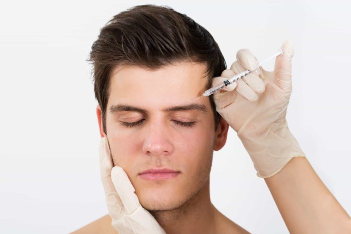 A man with closed eyes is receiving a botox injection in his forehead. The person administering the injection is wearing white gloves. The background is white and plain, underscoring its alternate uses beyond traditional settings.