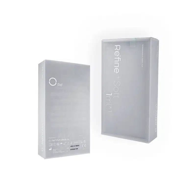 Two semi-transparent, rectangular boxes are shown against a white background. The boxes are light gray with minimal text and branding. One box is standing upright and the other is laying horizontally next to it. The text on the box reads "REFINE + SOFT.