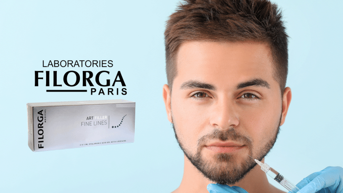 A man with short hair and a beard receives a Filorga filler injection in his lower face, administered by a gloved hand holding a hypodermic needle. Next to him is a box of Filorga Art Filler Fine Lines, with "Laboratoires Filorga Paris" written above it on a light blue background.