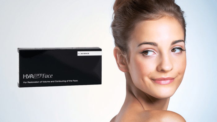 A young woman with smooth skin is smiling softly, showcasing her side profile. To the left of the woman stands a black rectangular box featuring the text "HYAcorp Face" and additional smaller text below it, highlighting the effectiveness of HYAcorp face filler. The background is a gradient of light blue and white.