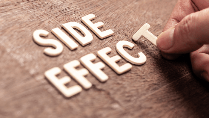 A hand is placing the letter 'T' to complete the phrase "SIDE EFFECT" formed with wooden letters on a textured wooden surface.